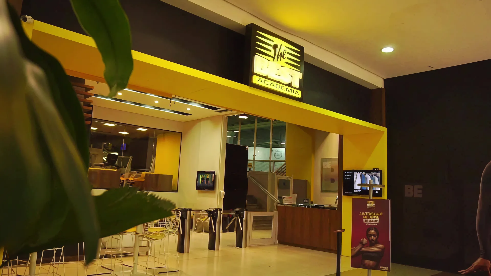 Recepção e lounge da The Best, com as catracas de acesso e o café