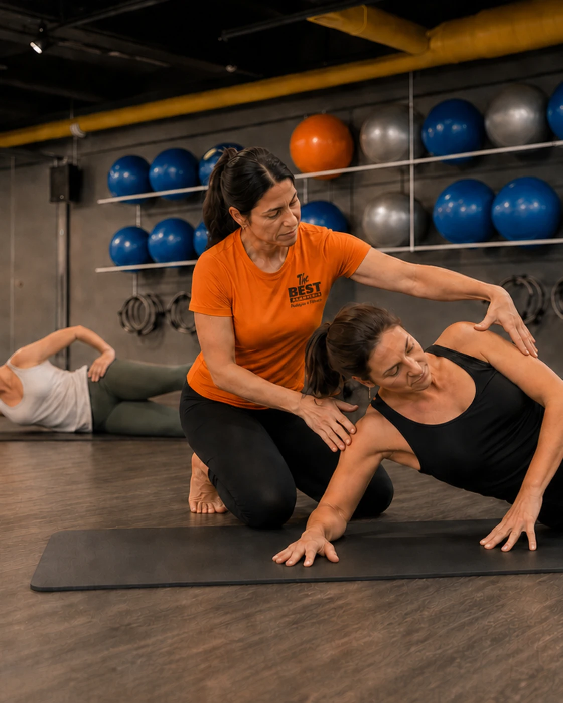 Educadora física da Academia The Best acompanha de perto uma aluna durante a aula de Pilates no solo